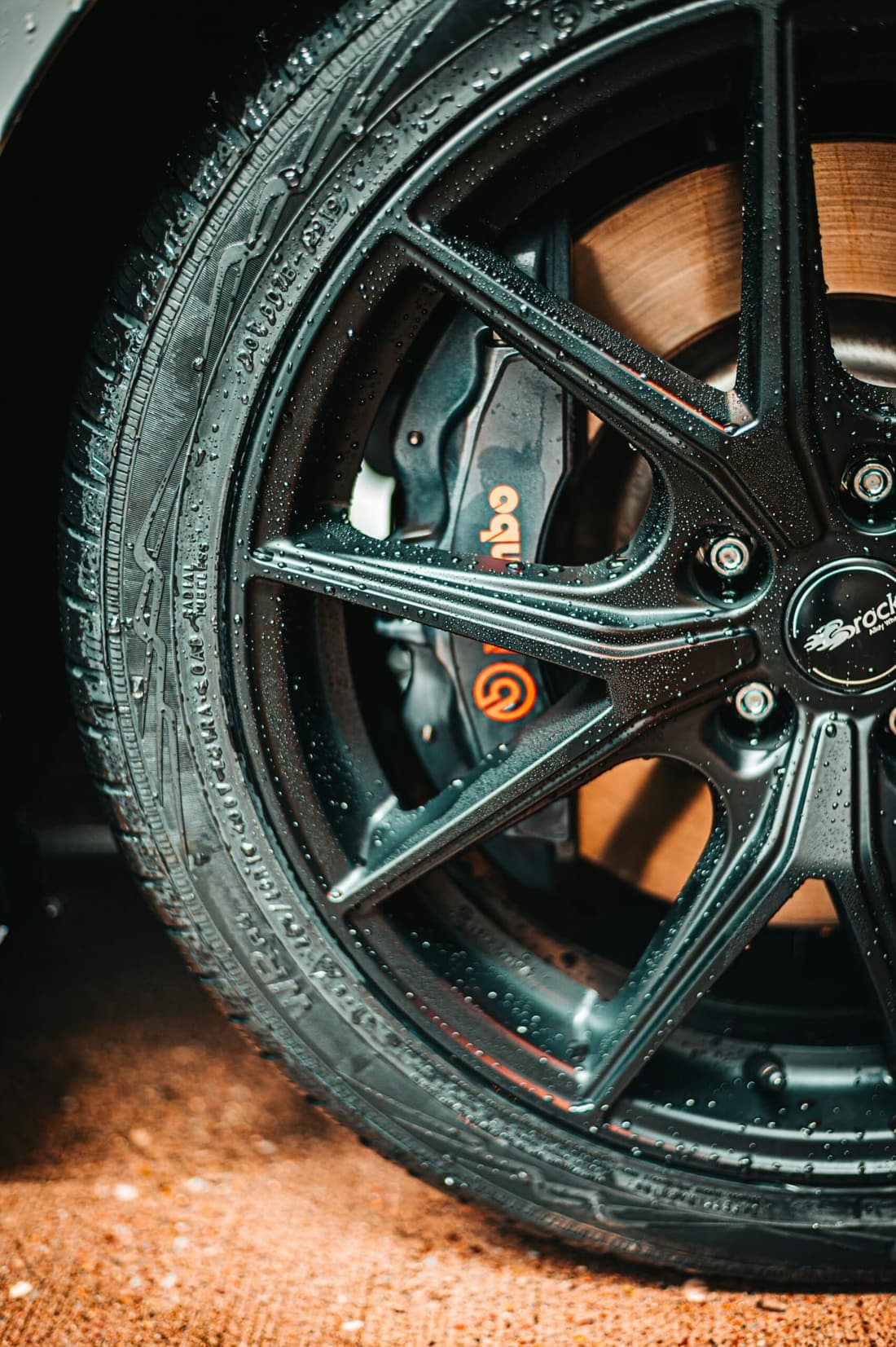 "Close-up of a wet car wheel featuring sleek rims and Brembo brake calipers, showcasing the premium detailing results from Premier Autos Detailing in West Plains, MO."