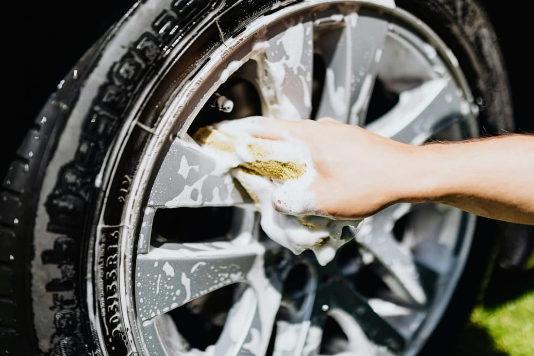 Hand cleaning a silver car rim with a yellow sponge on a bright day, showcasing DIY detailing techniques for car enthusiasts in West Plains, MO.