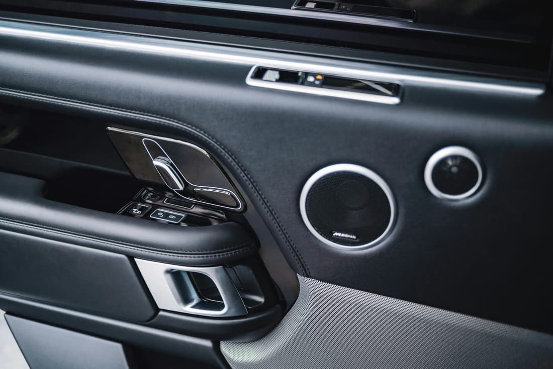 Close-up of a luxury car door panel featuring black leather, chrome accents, and premium speaker system.
