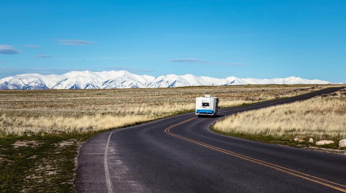 "An RV cruising confidently along a scenic road surrounded by vast fields and distant mountain ranges after a professional roof repair by Premier Autos Detailing."