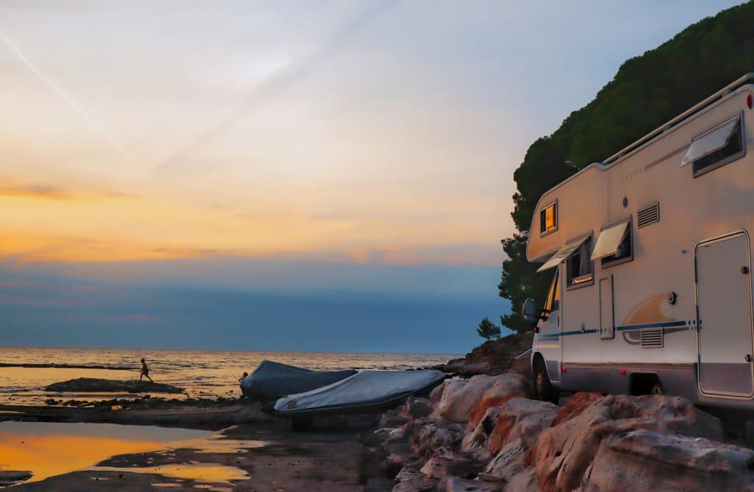 A camper RV parked by the coast at sunset, with open windows and a scenic ocean view in the background.