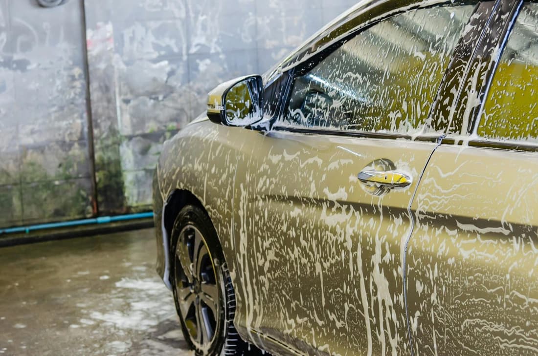 A gold car covered in thick soap suds during a professional car wash, highlighting the importance of thorough exterior detailing.