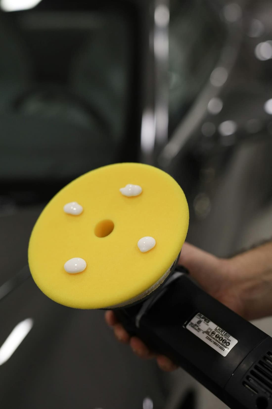 A professional-grade dual-action polisher with a yellow foam pad and polishing compound, ready for paint correction at Premier Autos Detailing.
