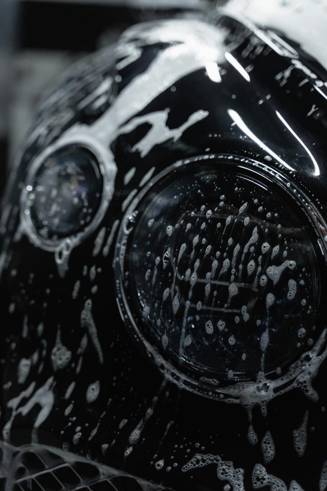 Close-up of a Bentley's headlight covered in rich car shampoo foam, showcasing Premier Autos Detailing's expert car care services in West Plains, MO.