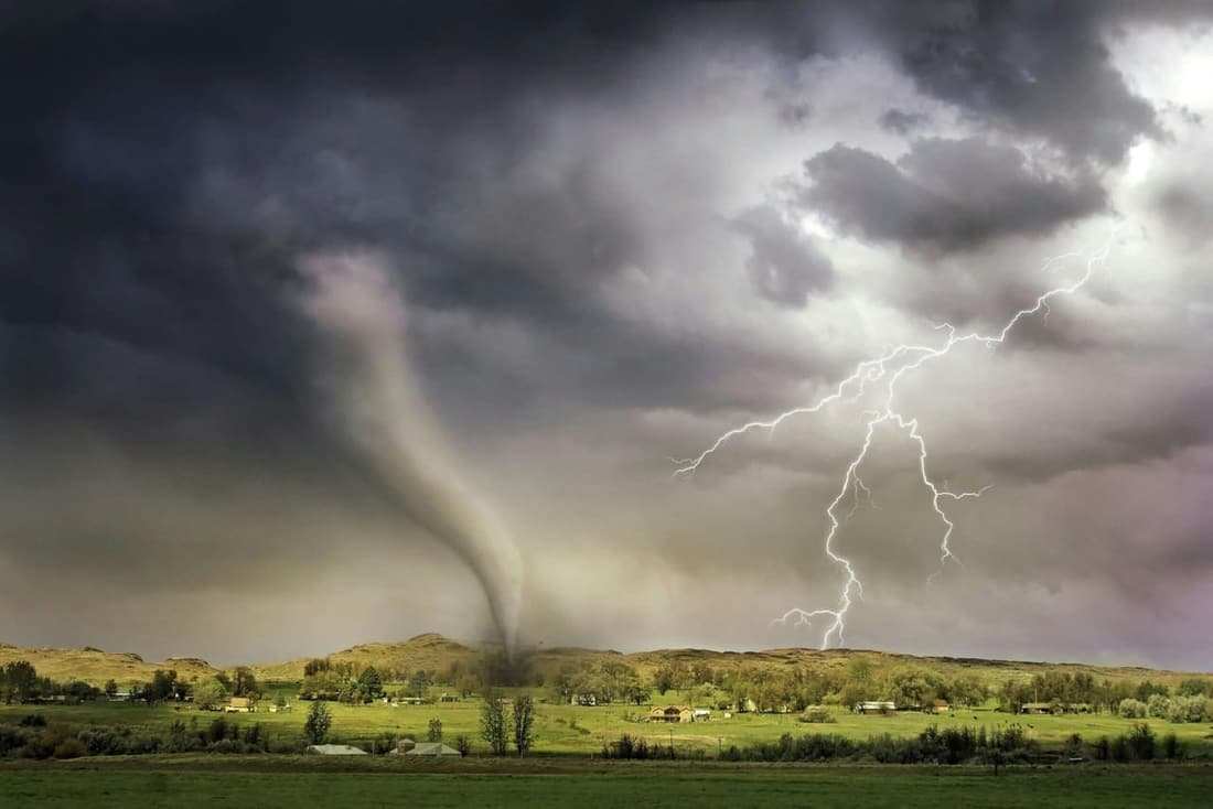 A powerful lightning strike illuminates a dark sky with a tornado in the background, showcasing the intense storm damage