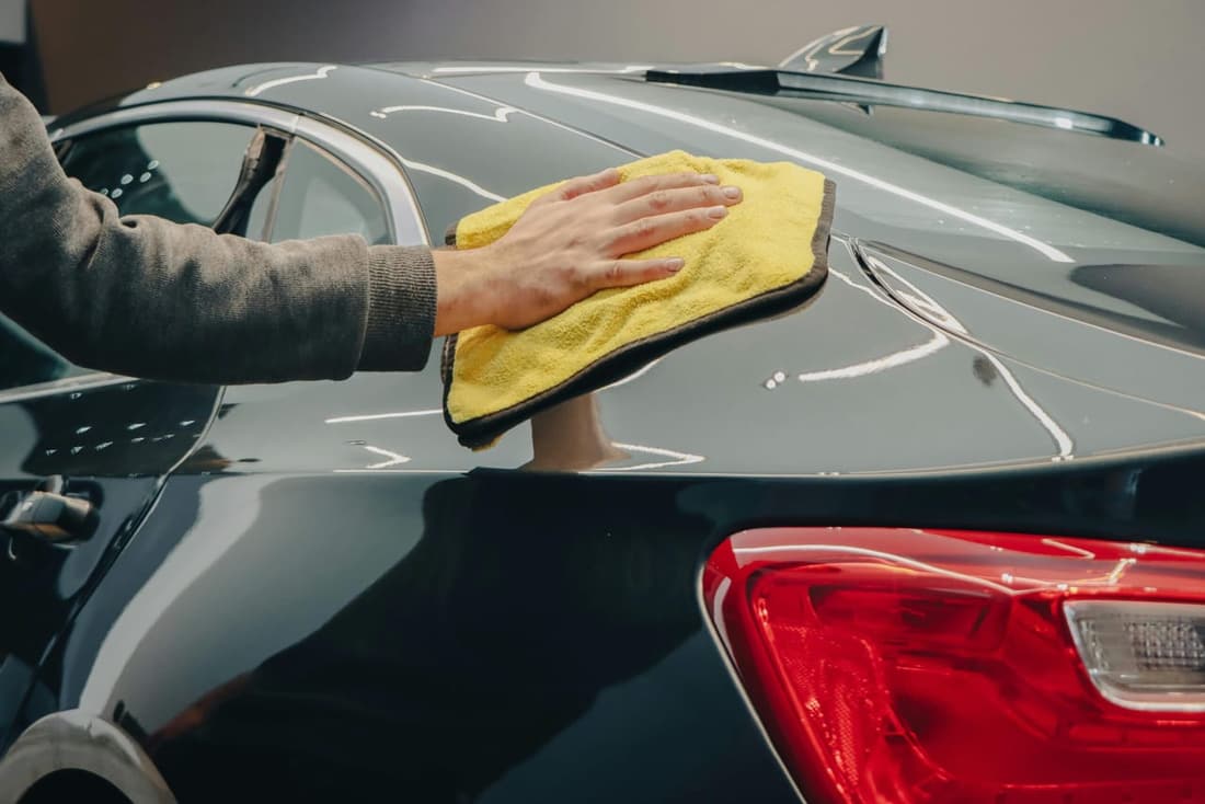Car detailing expert wiping down black car with microfiber towel