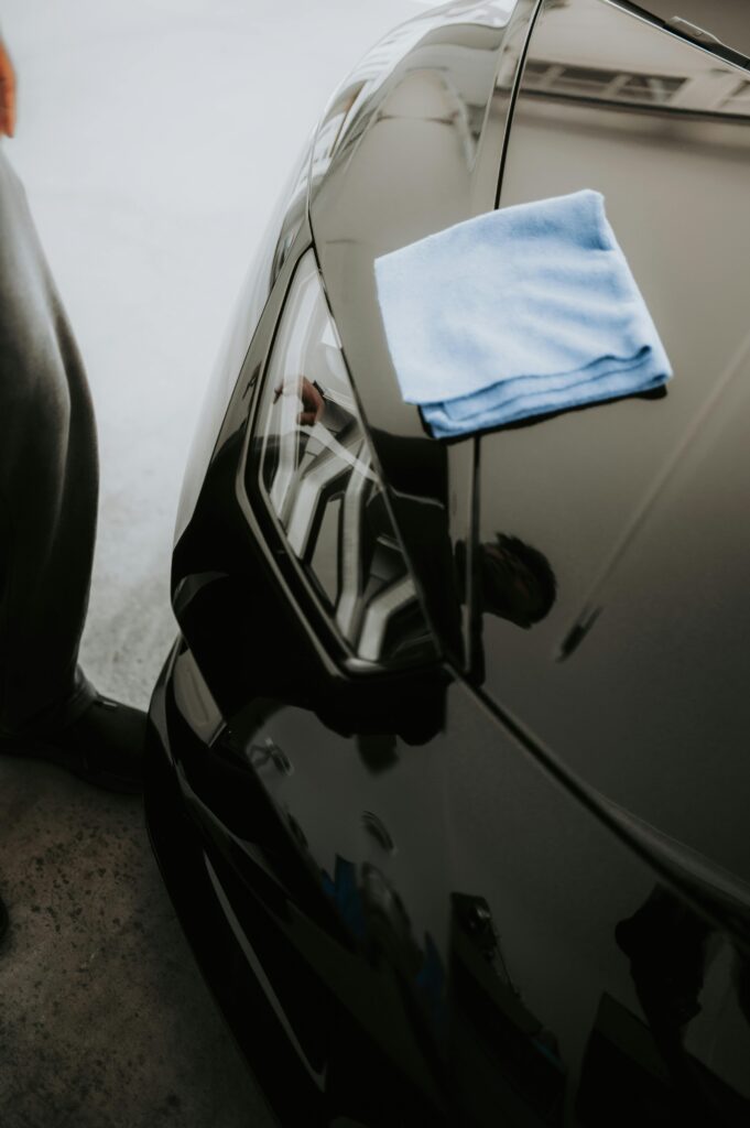 "Close-up of a luxury car's polished hood and headlight reflecting light, with a clean microfiber cloth on top, highlighting professional auto detailing, paint protection, and car care services in West Plains, MO."