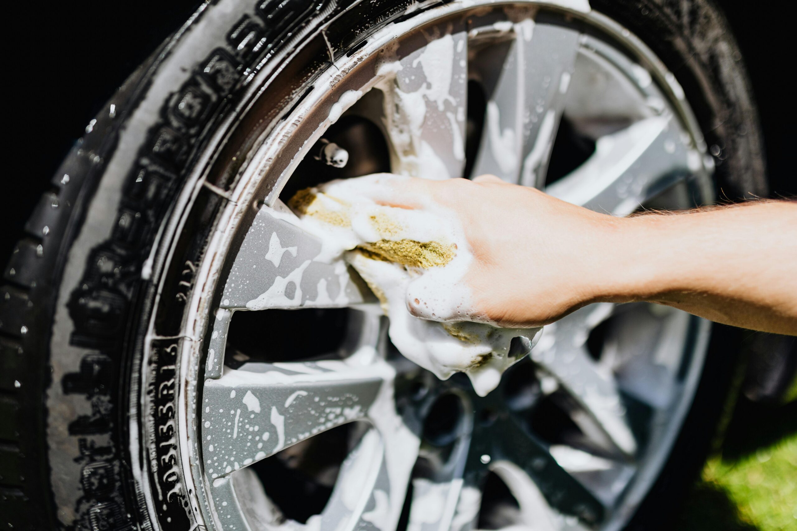 pexels-karolina-grabowska-4870705 Hand cleaning a silver car rim with a yellow sponge on a bright day, showcasing DIY detailing techniques for car enthusiasts in West Plains, MO.