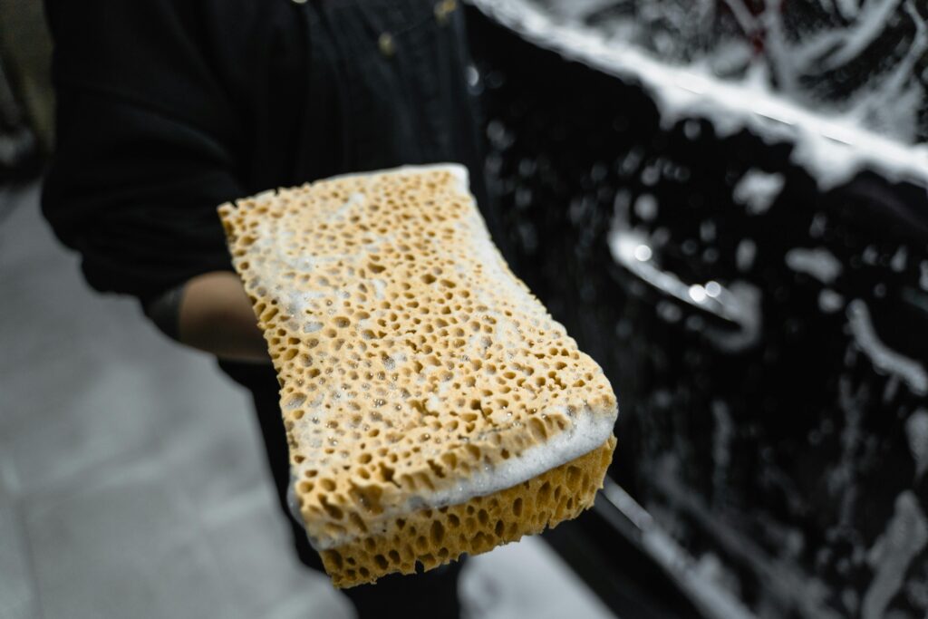 "Hand holding a wet, soapy sponge in front of a car, showcasing professional car cleaning techniques by Premier Autos Detailing in West Plains, MO."