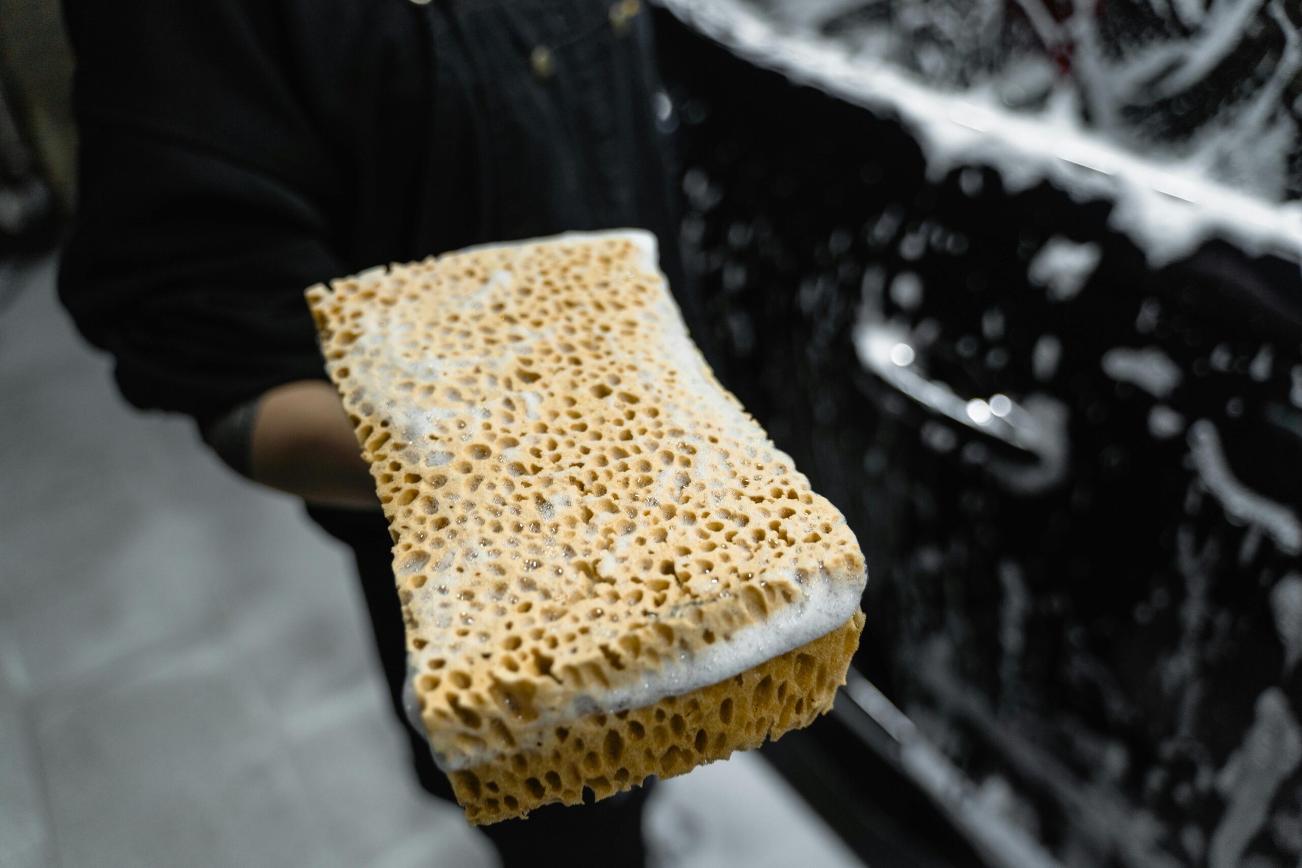 pexels-tima-miroshnichenko-6872575 "Hand holding a wet, soapy sponge in front of a car, showcasing professional car cleaning techniques by Premier Autos Detailing in West Plains, MO."