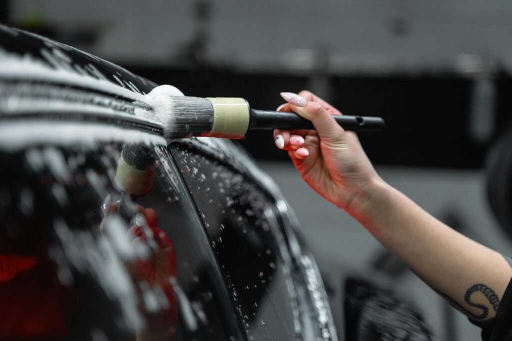 Close-up of a professional detailer using a brush to clean a soapy car exterior, ensuring precision and shine during the detailing process.