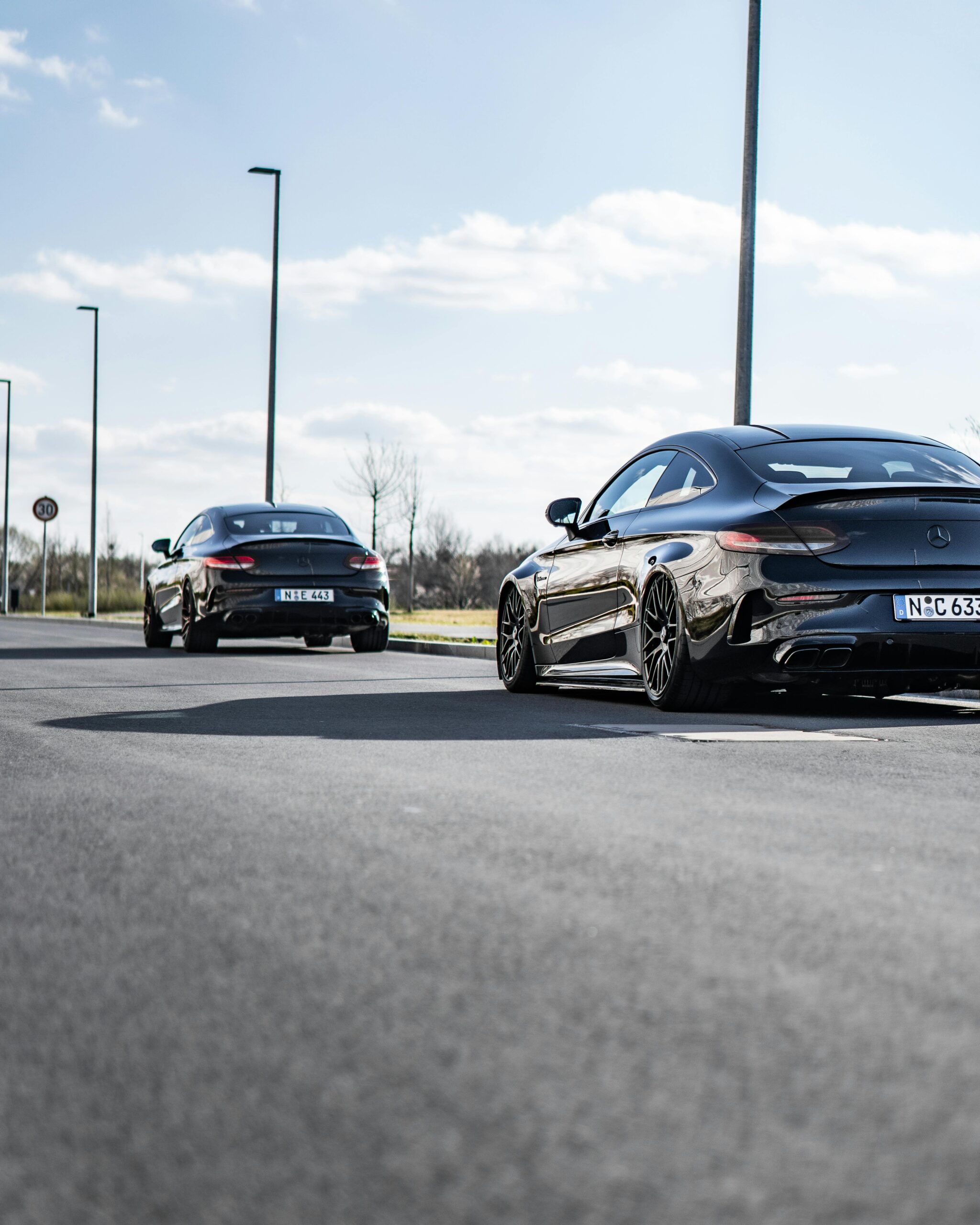 pexels-ibragraphics-10224505 Two professionally detailed black Mercedes-Benz coupes with a flawless shine, parked on a smooth road under a bright sky.