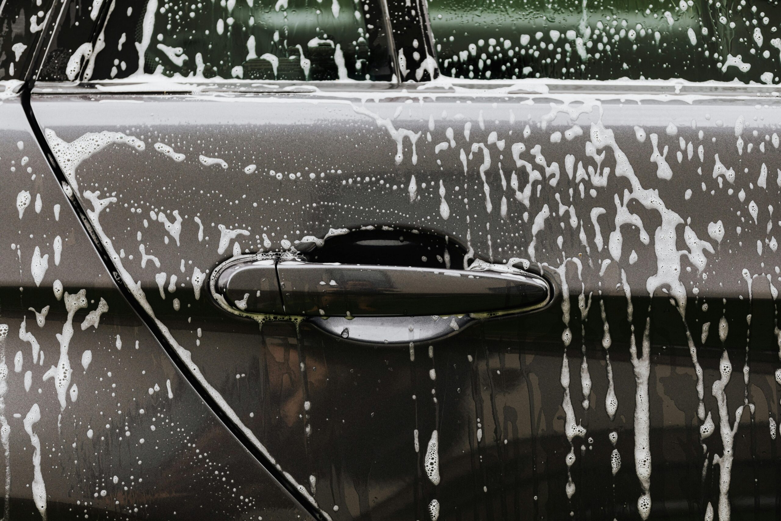 pexels-karolina-grabowska-4870724 Close-up of a car door covered in soapy water during a wash, highlighting the importance of regular detailing for paint protection.