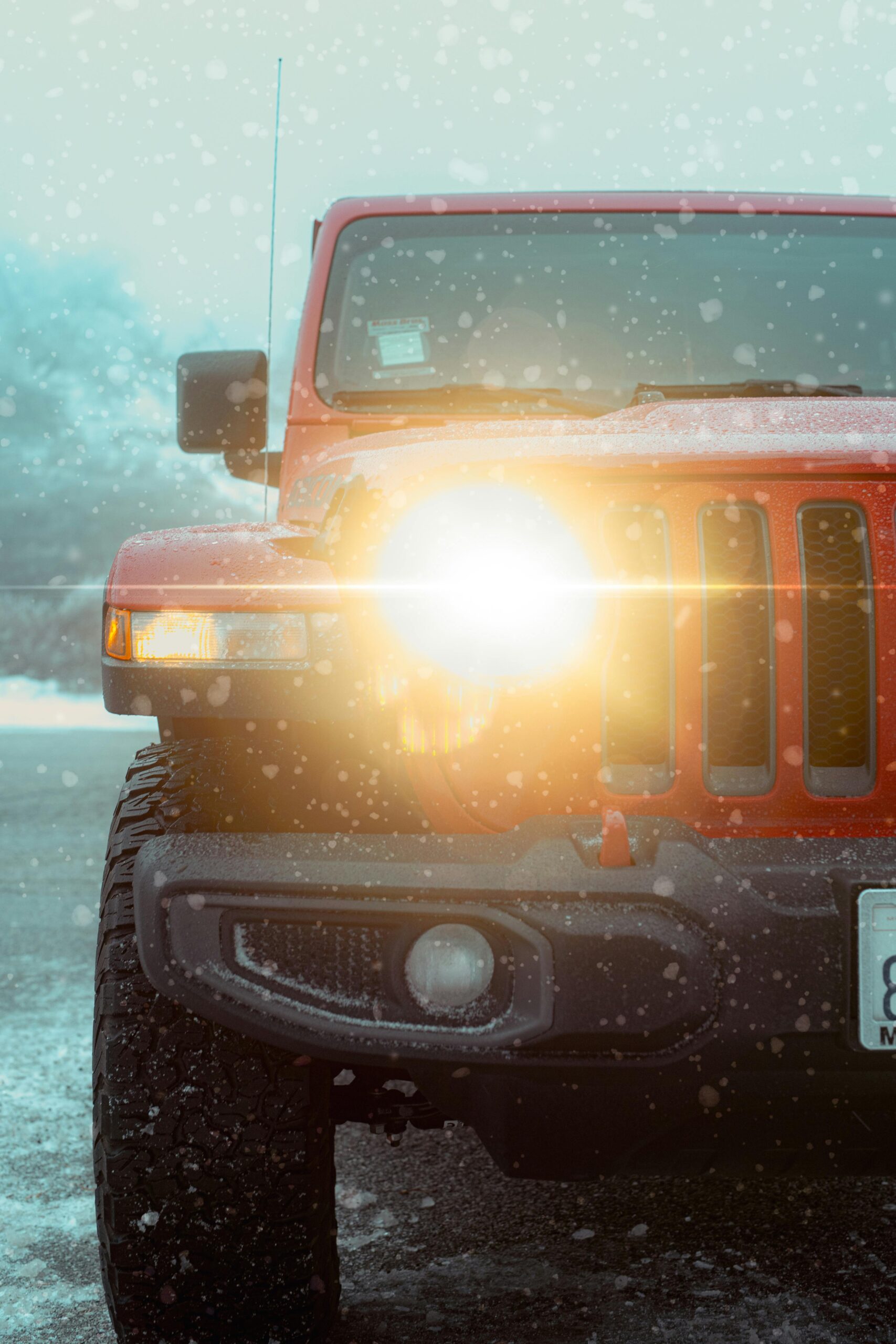 pexels-smepictures-10656077 A red Jeep with headlights on, covered in snow during a winter storm.