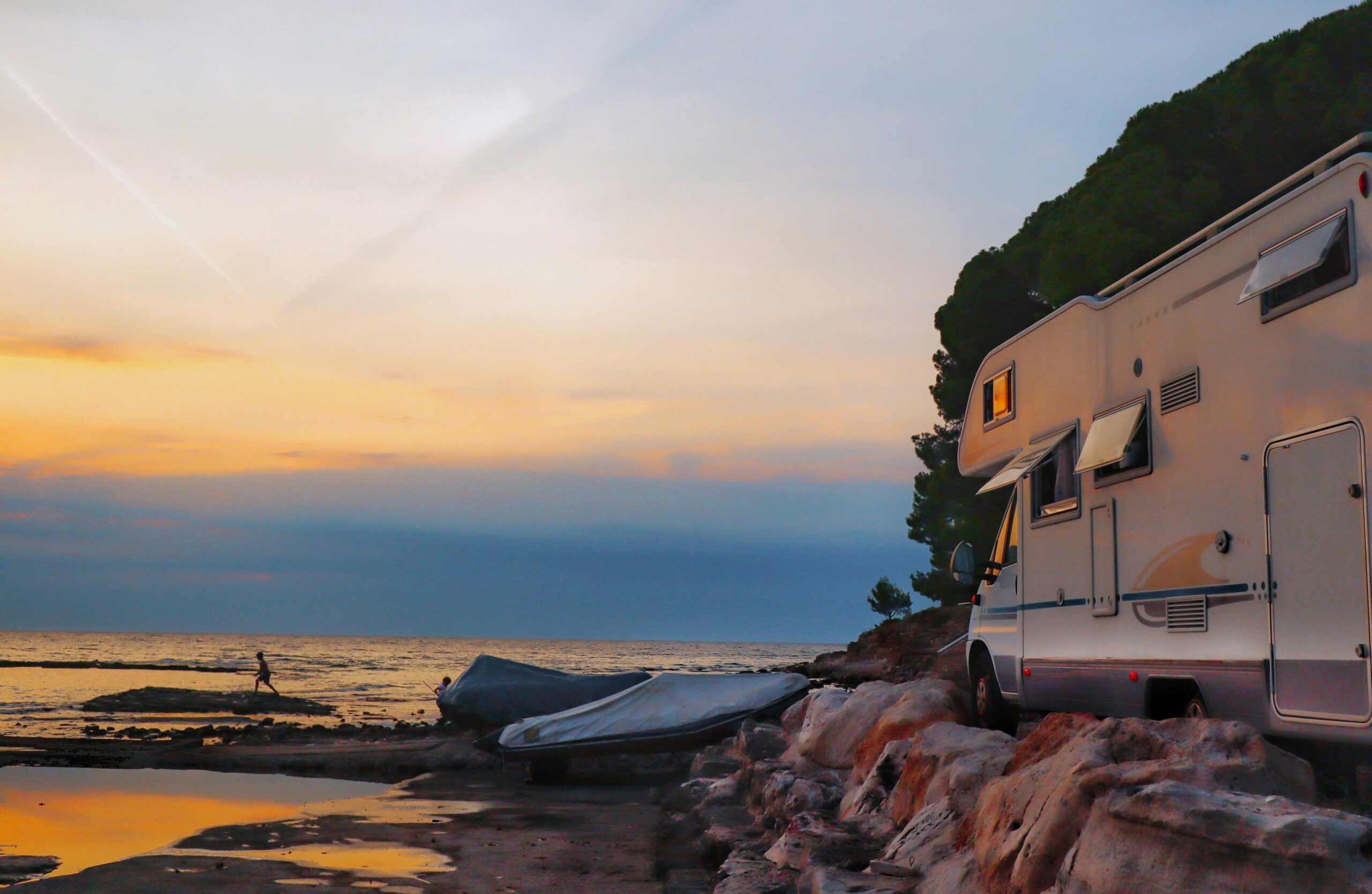 pexels-damir-13134378 A camper RV parked by the coast at sunset, with open windows and a scenic ocean view in the background.