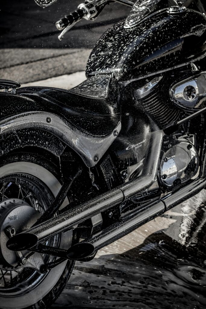 Close-up of a black motorcycle being washed with soap and water, emphasizing professional detailing.