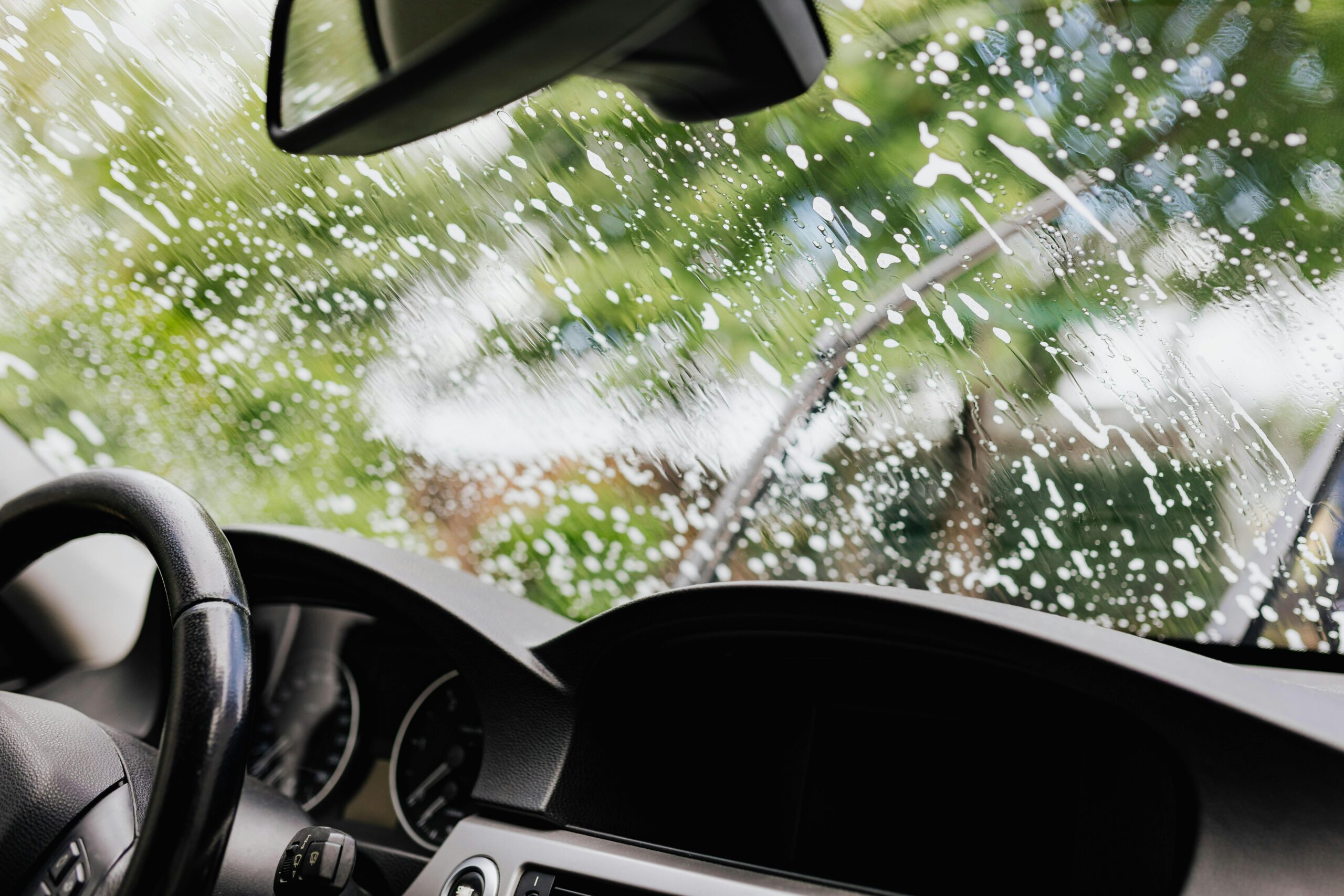 pexels-karolina-grabowska-4870706 Interior view of a car during a windshield wash with soap suds and wipers in motion.