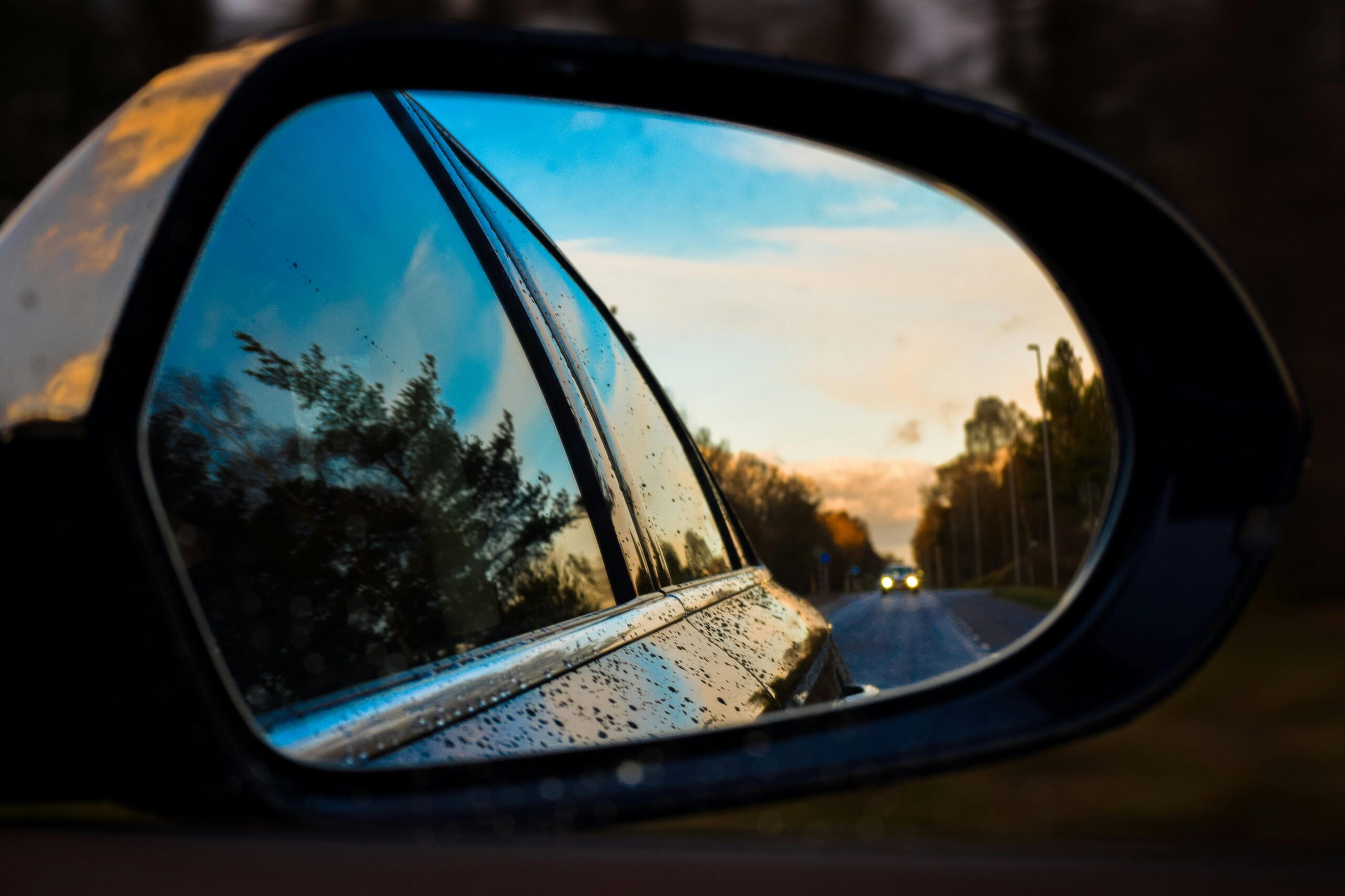 pexels-pixabay-461890 A car’s side mirror reflecting a clean road with a sunset sky, water droplets visible on the mirror and car body.