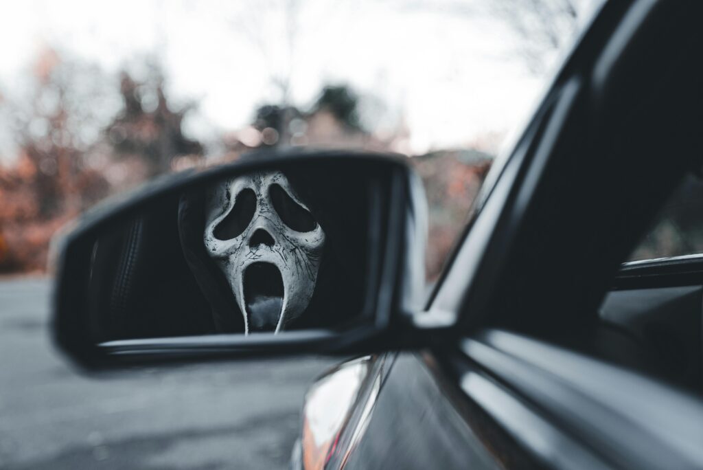 Horror mask reflection in a car side mirror during Halloween.
